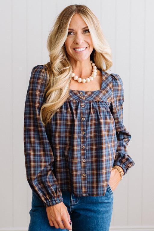 Blonde woman in a brightly lit studio wearing a PLAID SQUARE NECK BUTTON CLOSURE FRONT LONG SLEEVE BLOUSE  WITH DARK JEANS AND BROWN BOOTS.
