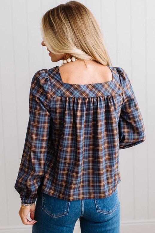 Blonde woman in a brightly lit studio wearing a PLAID SQUARE NECK BUTTON CLOSURE FRONT LONG SLEEVE BLOUSE  WITH DARK JEANS AND BROWN BOOTS.