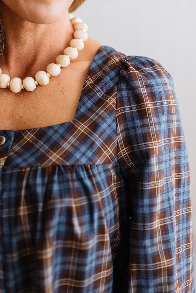 Blonde woman in a brightly lit studio wearing a PLAID SQUARE NECK BUTTON CLOSURE FRONT LONG SLEEVE BLOUSE  WITH DARK JEANS AND BROWN BOOTS.