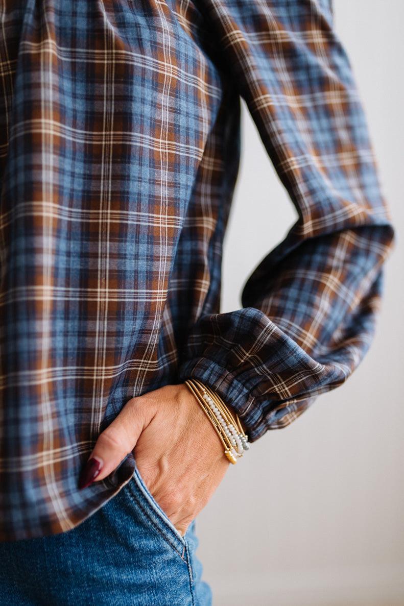 Blonde woman in a brightly lit studio wearing a PLAID SQUARE NECK BUTTON CLOSURE FRONT LONG SLEEVE BLOUSE  WITH DARK JEANS AND BROWN BOOTS.