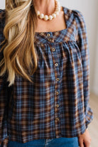 Blonde woman in a brightly lit studio wearing a PLAID SQUARE NECK BUTTON CLOSURE FRONT LONG SLEEVE BLOUSE  WITH DARK JEANS AND BROWN BOOTS.