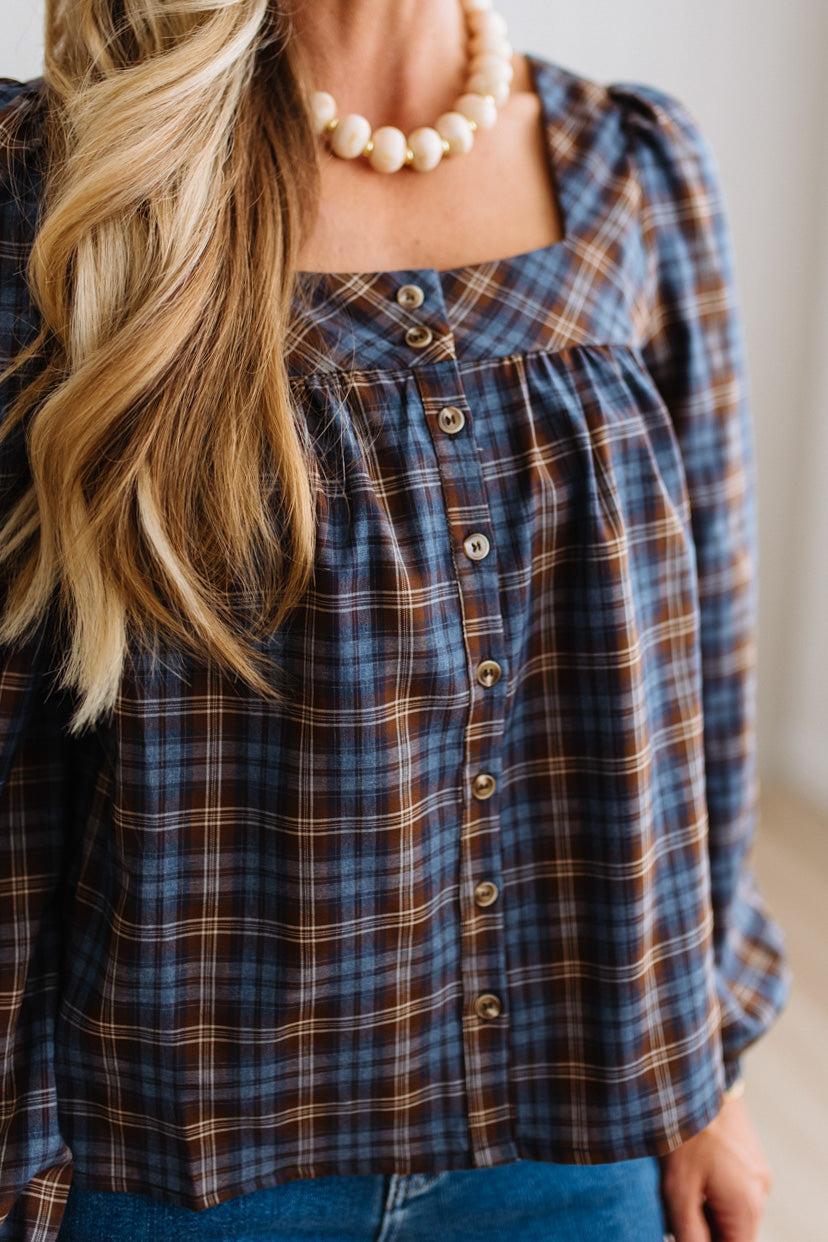 Blonde woman in a brightly lit studio wearing a PLAID SQUARE NECK BUTTON CLOSURE FRONT LONG SLEEVE BLOUSE  WITH DARK JEANS AND BROWN BOOTS.
