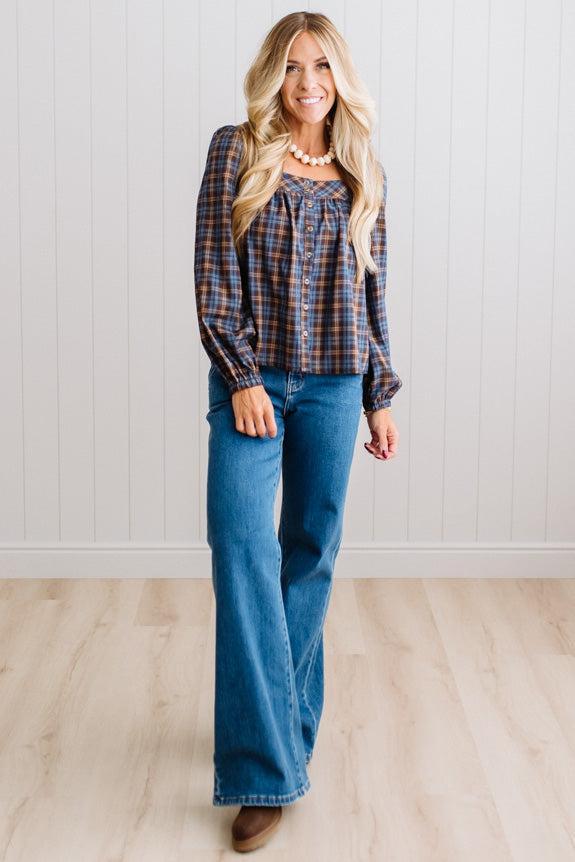 Blonde woman in a brightly lit studio wearing a PLAID SQUARE NECK BUTTON CLOSURE FRONT LONG SLEEVE BLOUSE  WITH DARK JEANS AND BROWN BOOTS.