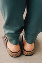 Woman wearing ash jade joggers zoomed in to show brown slip on sandals with double strap and brushed gold buckles.