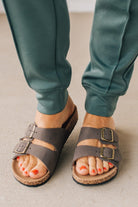 Woman wearing ash jade joggers zoomed in to show brown slip on sandals with double strap and brushed gold buckles.