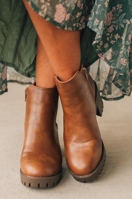 Brown leather boots worn with a floral dress on a neutral background