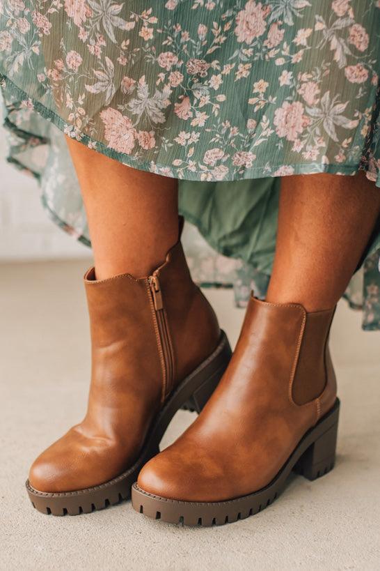 Brown leather ankle boots worn with a floral dress on a neutral background