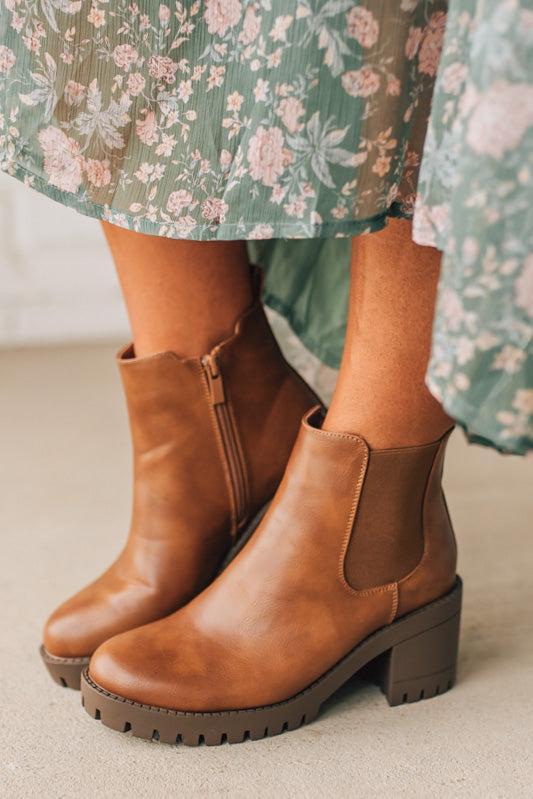 Brown leather boots worn with a floral dress on a neutral background
