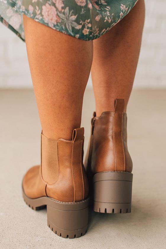 Brown ankle boots worn with a floral dress on a neutral background