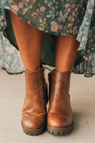 Brown leather boots worn with a floral dress on a neutral background