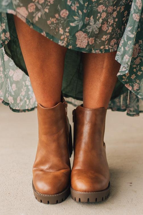 Brown leather boots worn with a floral dress on a neutral background