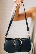 Woman holding a small black handbag with large silver buckle accent and silver hardware