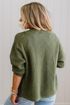 Person wearing a green knitted sweater from behind against a light background