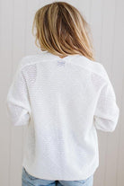 Person wearing a white knitted cardigan against a light wooden panel background
