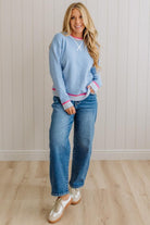 Woman wearing a light blue sweater and jeans standing against a white paneled wall.