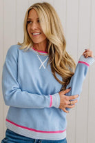 Woman wearing a light blue sweater with pink and white accents, standing against a plain background.
