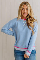 Woman wearing a light blue sweater with pink accents against a white wall