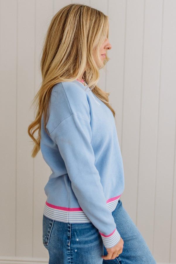 Woman wearing a light blue sweatshirt with pink trim against a white wall