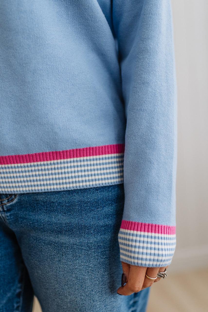 Light blue sweater with pink and white checkered cuffs and hem on a plain background