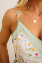 Woman wearing a light green sleeveless top with floral pattern and gold necklace.