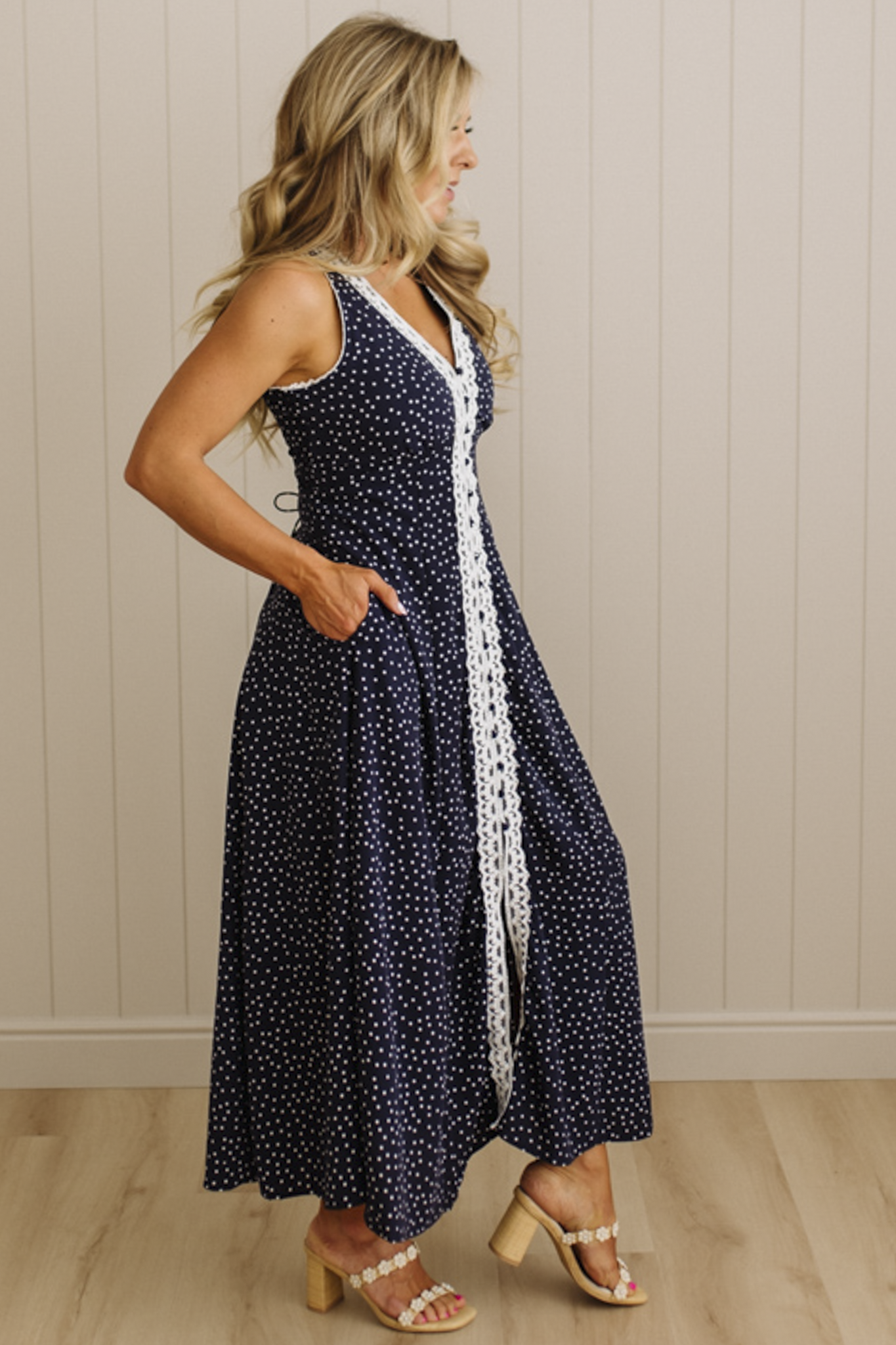 Woman wearing a navy blue dress with white polka dots and a white stripe standing against a beige wall.