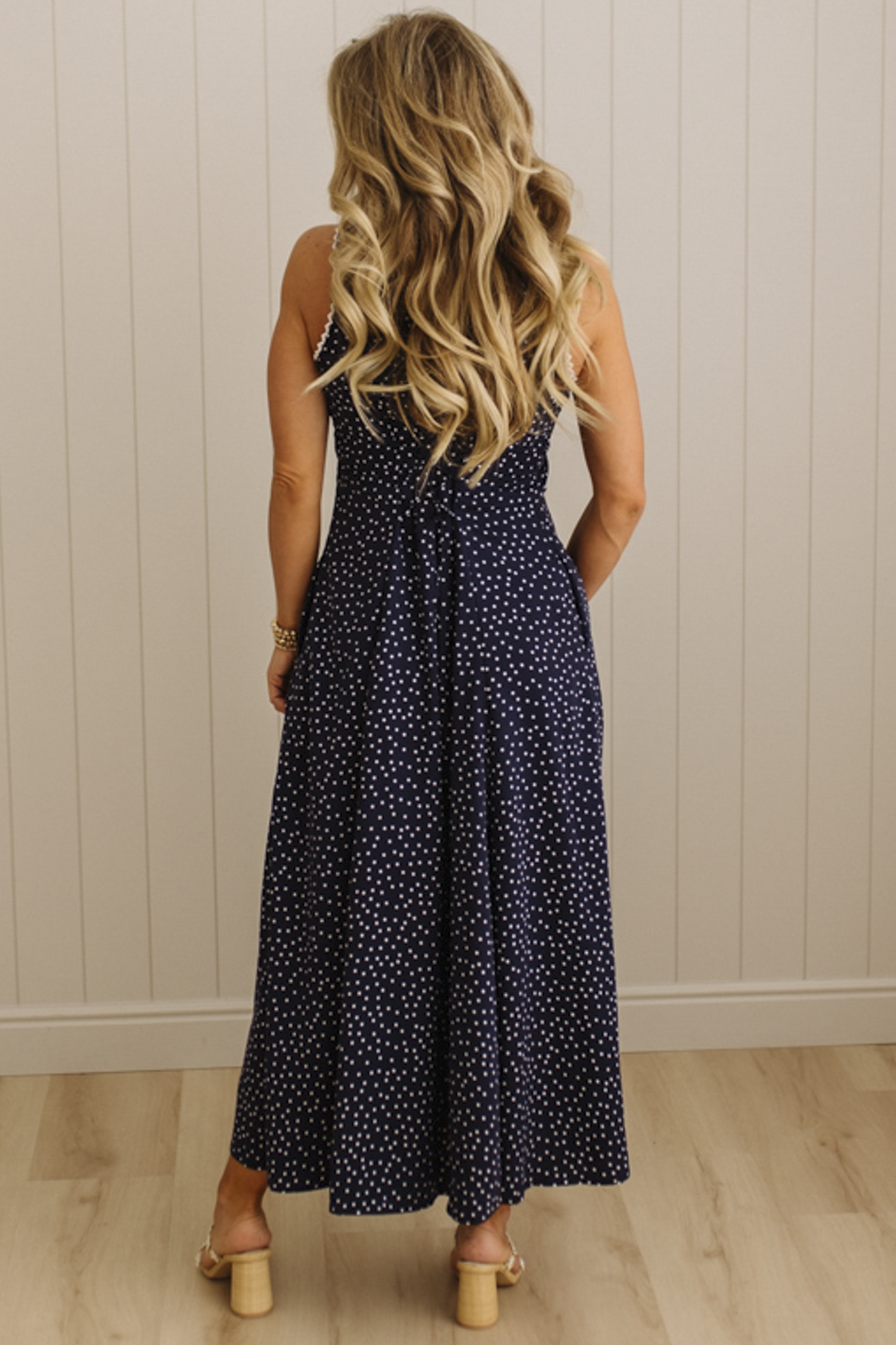 Woman wearing a navy blue polka dot dress with a white wall background