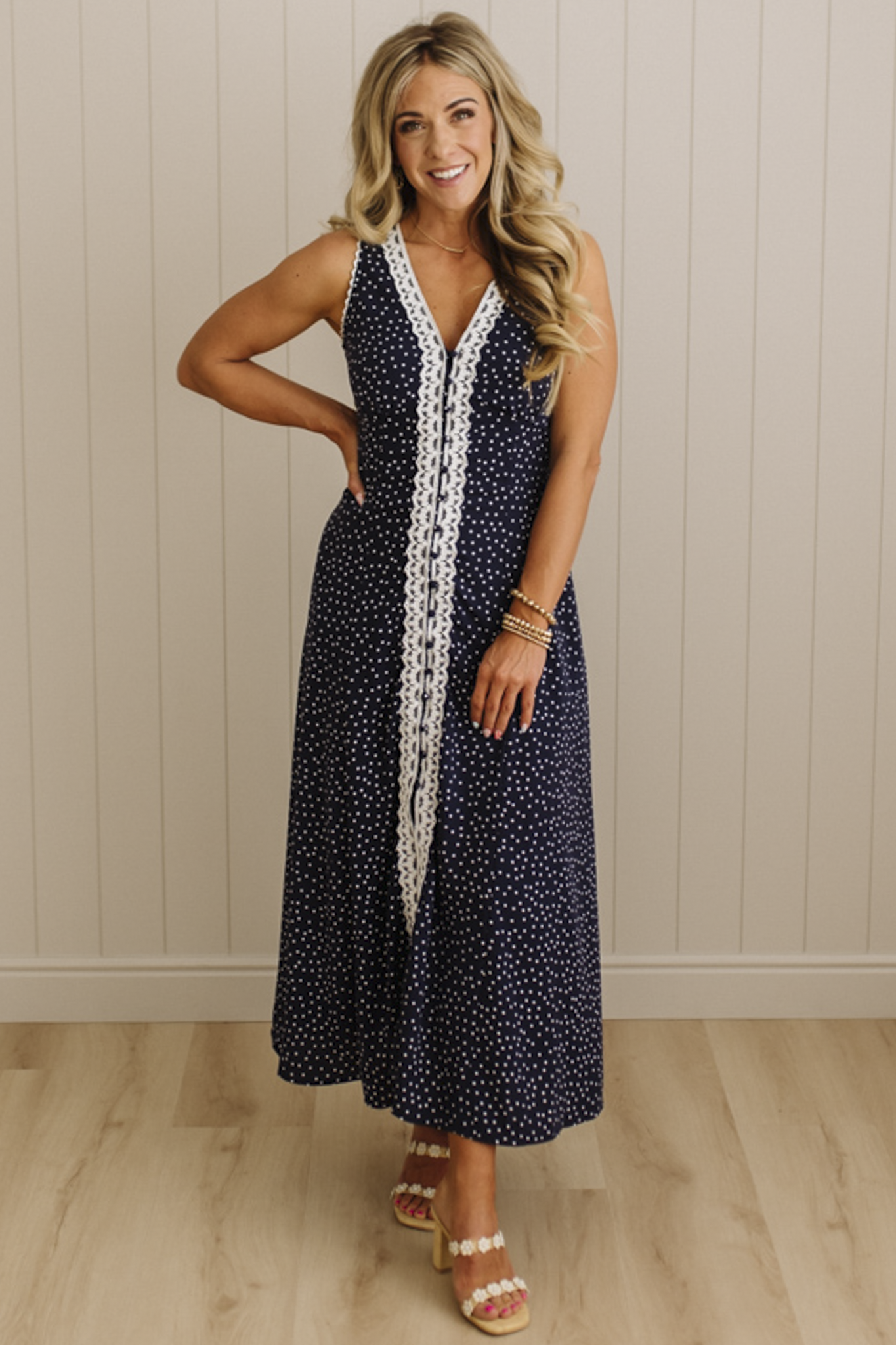 Woman wearing a navy dress with white polka dots and lace details against a beige wall.