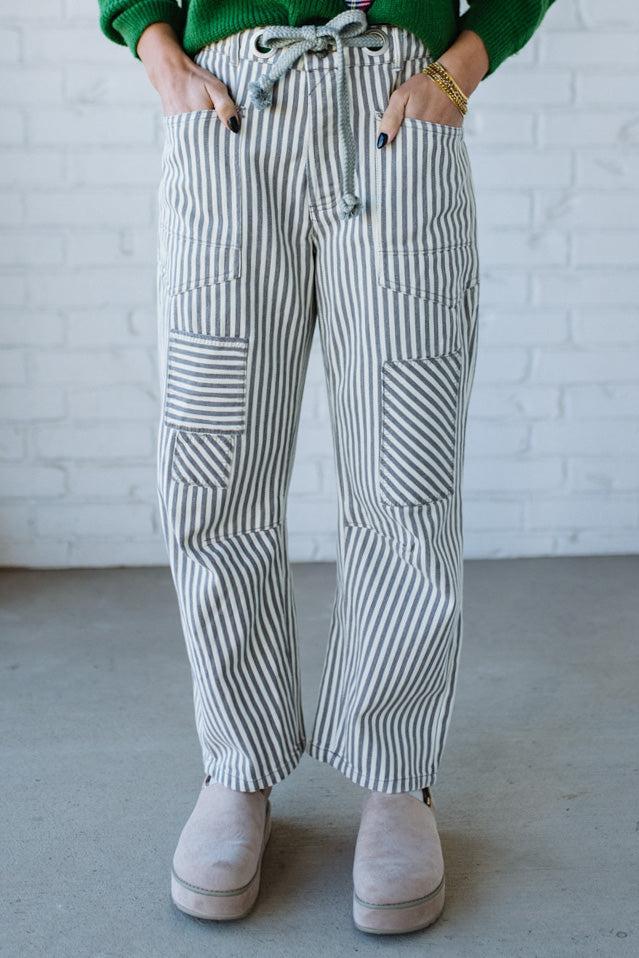 Woman wearing grey and cream vertical stiriped barrel cut jeans with a drawstring waist.