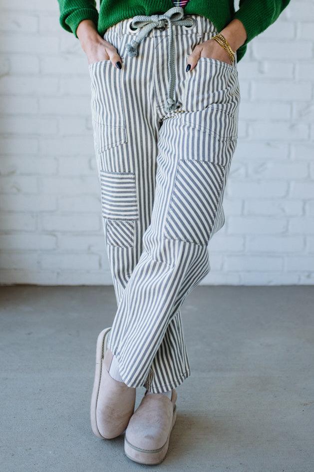 Woman wearing grey and cream vertical stiriped barrel cut jeans with a drawstring waist.
