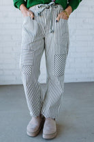 Woman wearing grey and cream vertical stiriped barrel cut jeans with a drawstring waist.