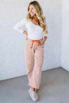 Woman wearing a white top and striped pants with an orange belt against a white brick wall.
