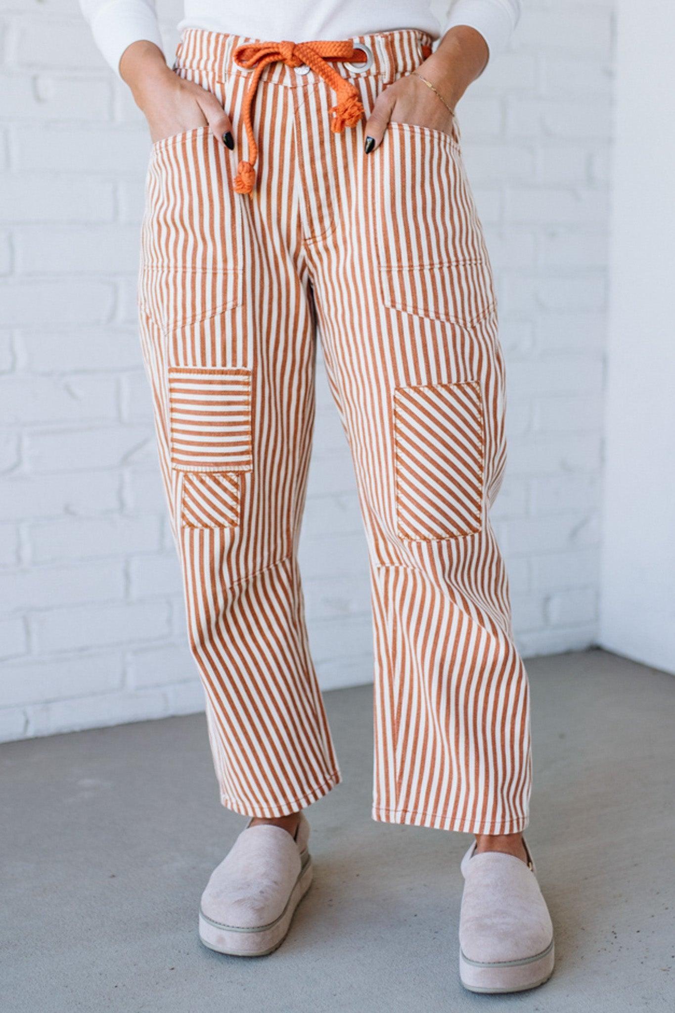Person wearing striped pants with an orange drawstring, standing against a white brick wall.