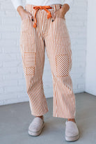 Person wearing striped pants with an orange drawstring, standing against a white brick wall.