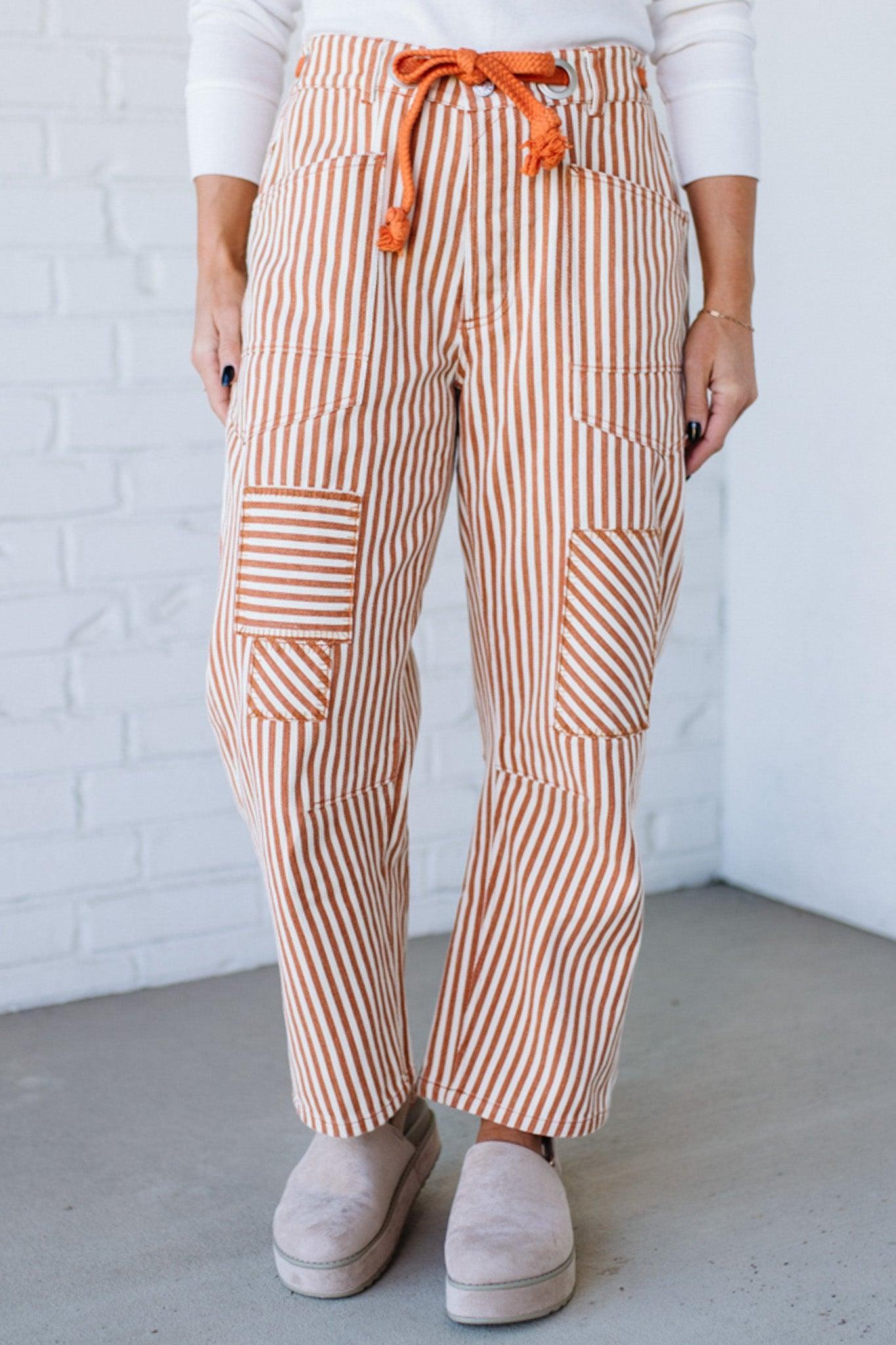 Person wearing orange and white striped pants with an orange drawstring against a white brick wall.