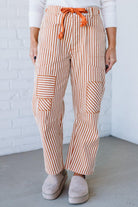 Person wearing orange and white striped pants with an orange drawstring against a white brick wall.
