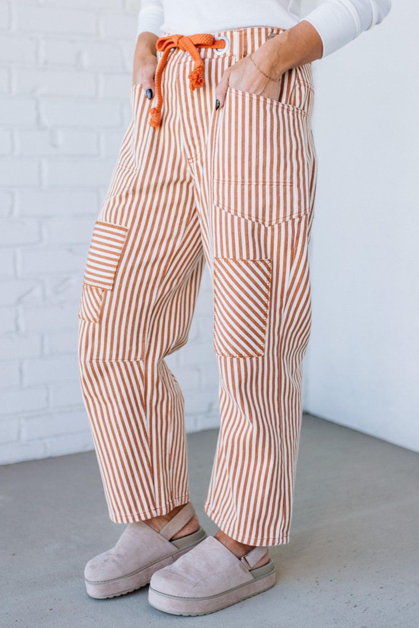 Person wearing brown and white striped pants with orange drawstring against a white brick wall.