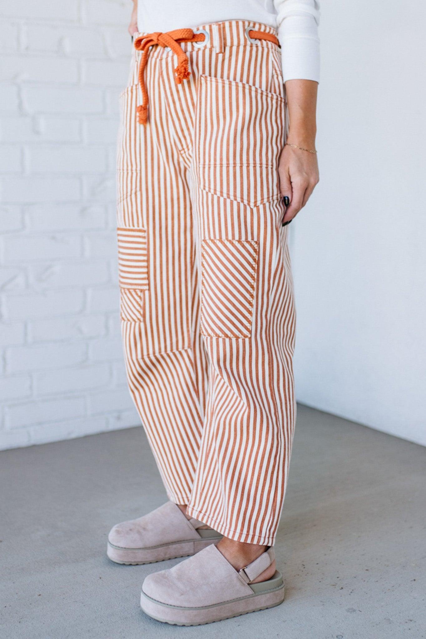 Person wearing striped pants with orange drawstring and beige platform shoes against a white brick wall.