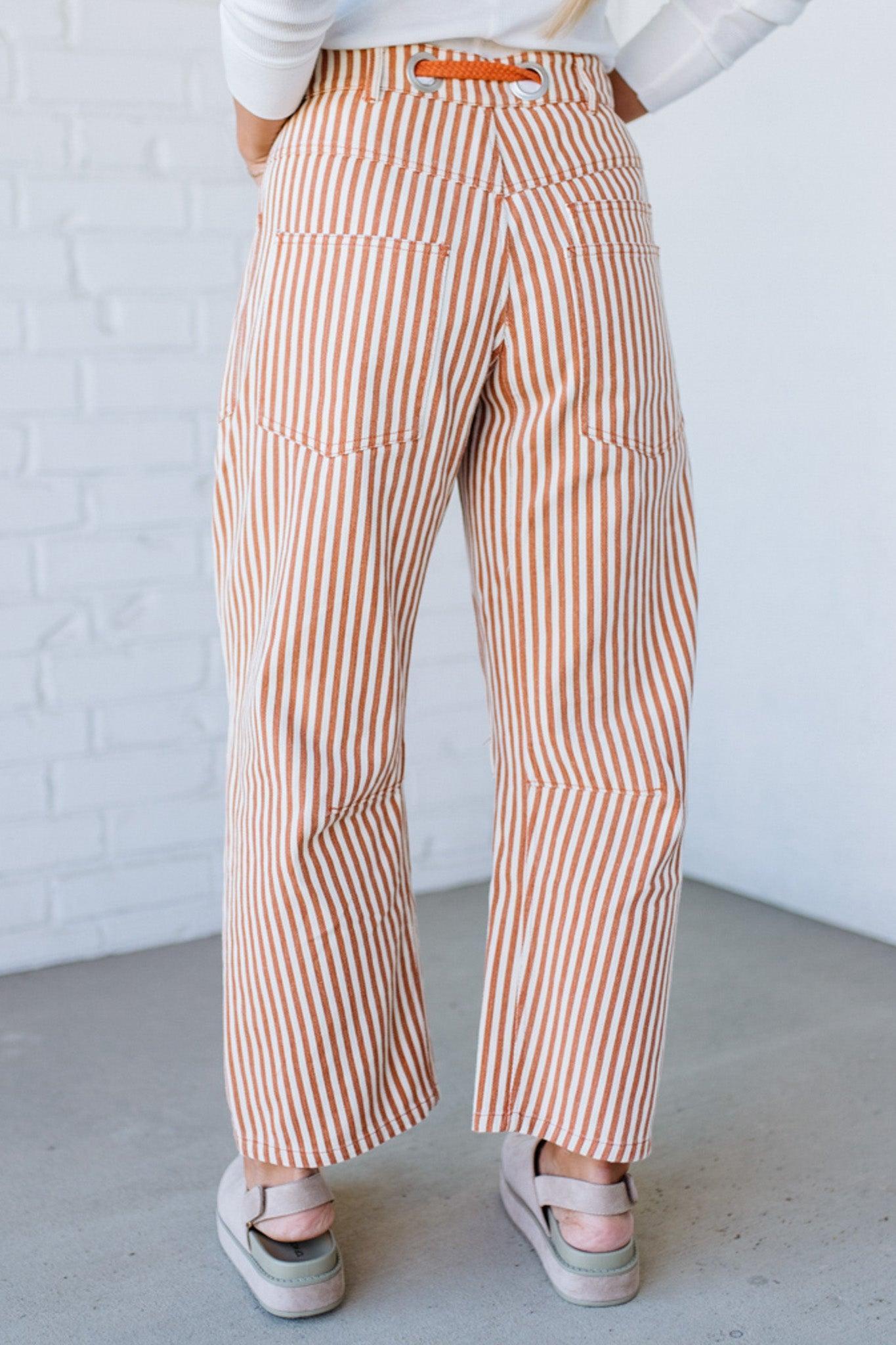 Person wearing brown and white striped pants against a white brick wall.