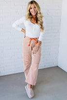 Woman wearing a white top and striped pants with an orange belt against a white brick wall.