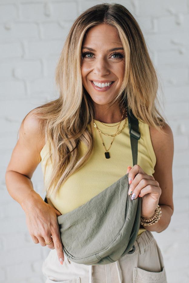Blonde woman in a yellow tank wearing an olive green nylon slingbag.