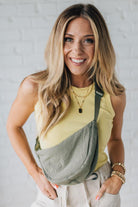 Blonde woman in a yellow tank wearing an olive green nylon slingbag.