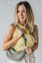 Blonde woman in a yellow tank wearing an olive green nylon slingbag.