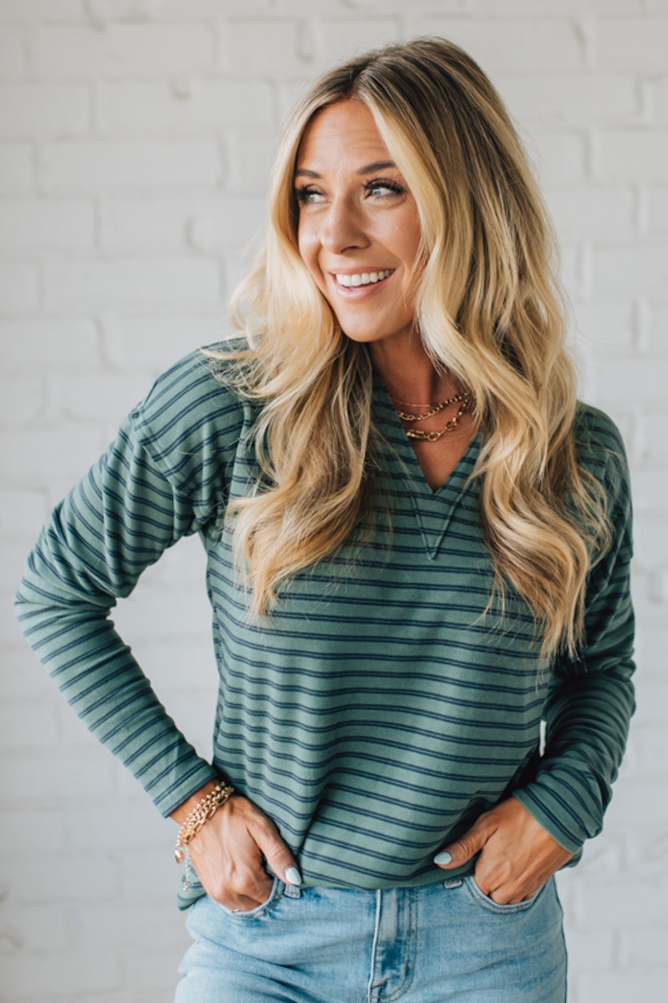 Woman wearing a green striped long-sleeve top against a white brick wall.