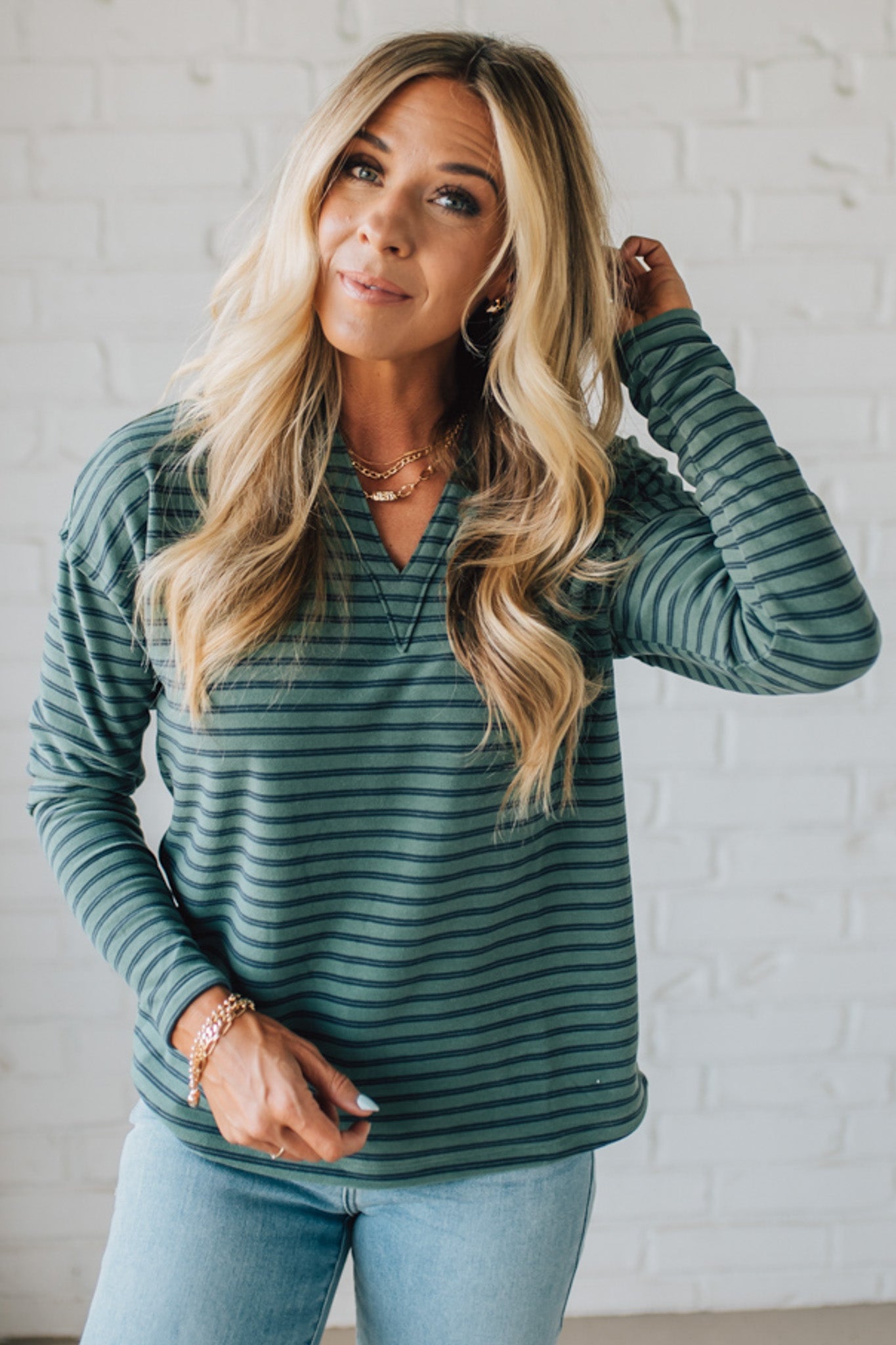 Woman wearing a green striped long-sleeve top against a white brick wall.