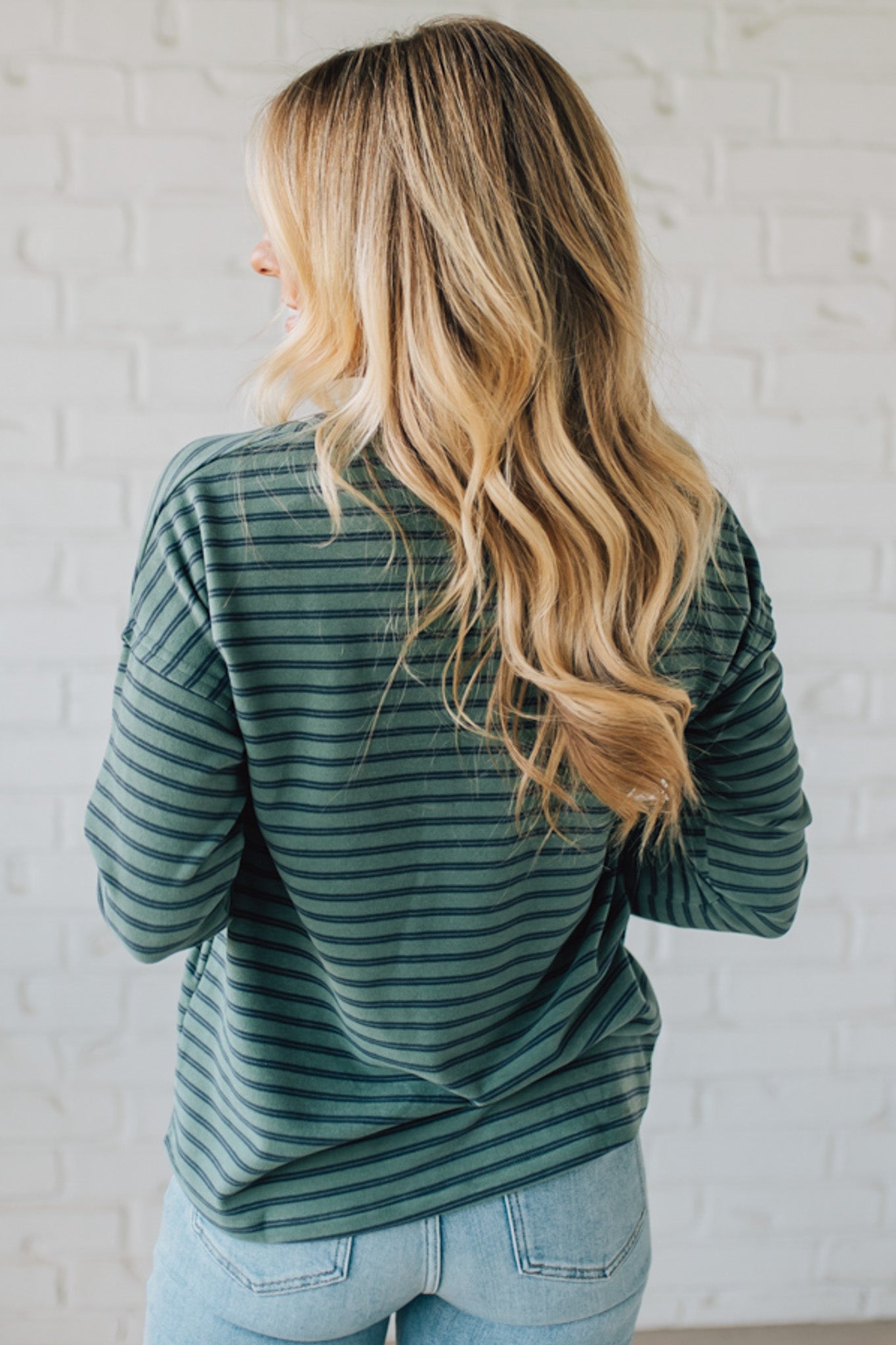 Person wearing a green striped sweater against a white brick wall