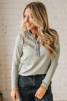 Woman wearing a gray long-sleeve top with a white brick wall background
