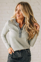 Woman wearing a light gray long-sleeve top with a zipper detail against a white brick wall.