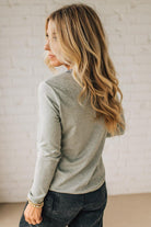 Woman wearing a gray long-sleeve top and dark jeans against a light background