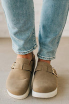 Beige loafers worn with light blue jeans on a neutral background