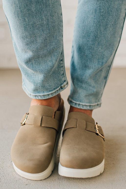 Beige loafers worn with light blue jeans on a neutral background